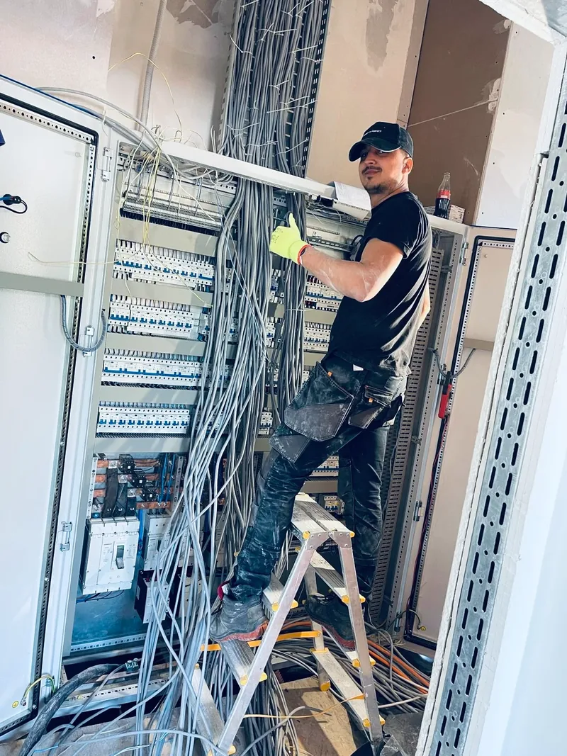 Electrician pe scară, racordând cablurile într-un tablou
